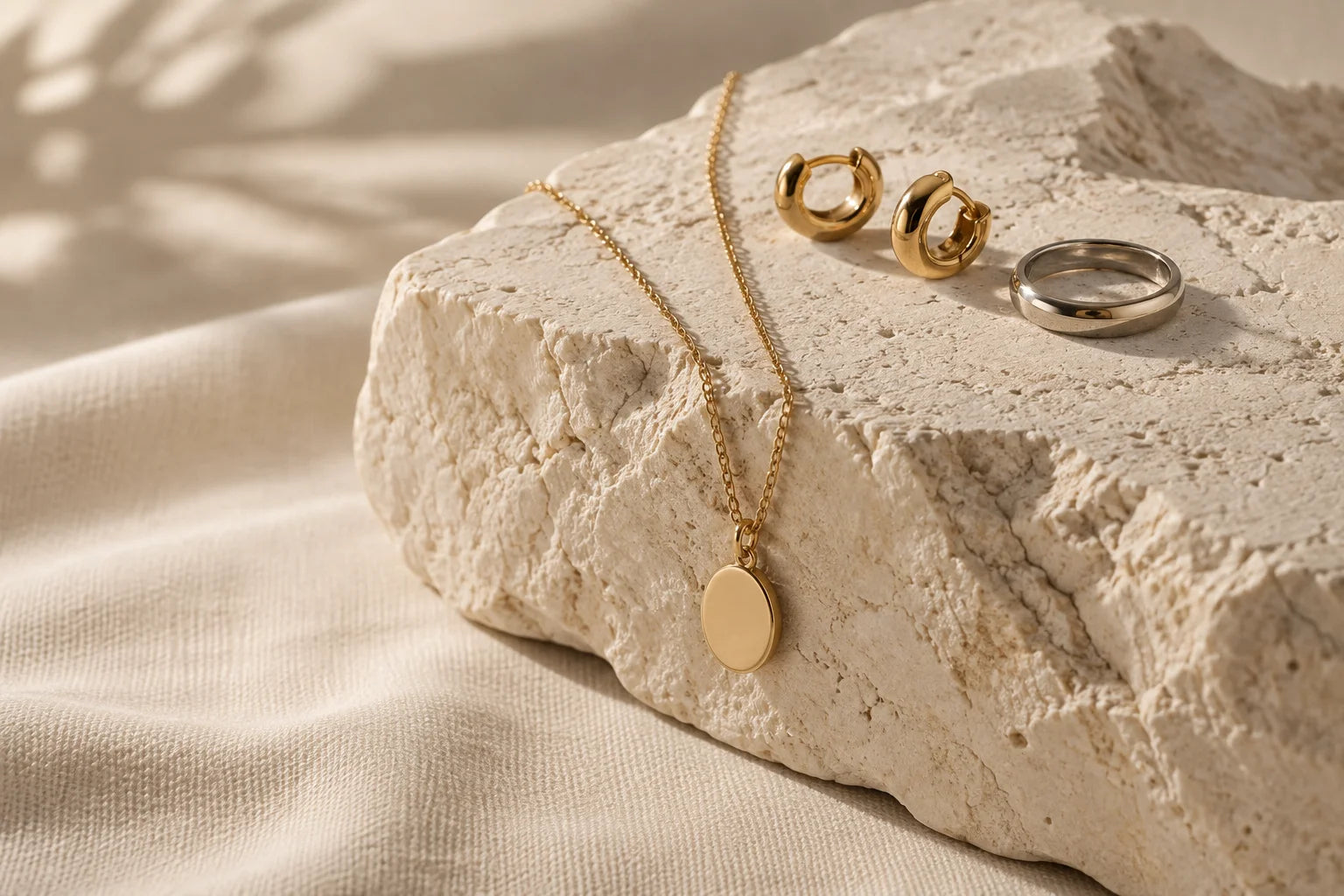 Demo composition of gold-tone pendant and hoops beside a silver-tone band on warm stone